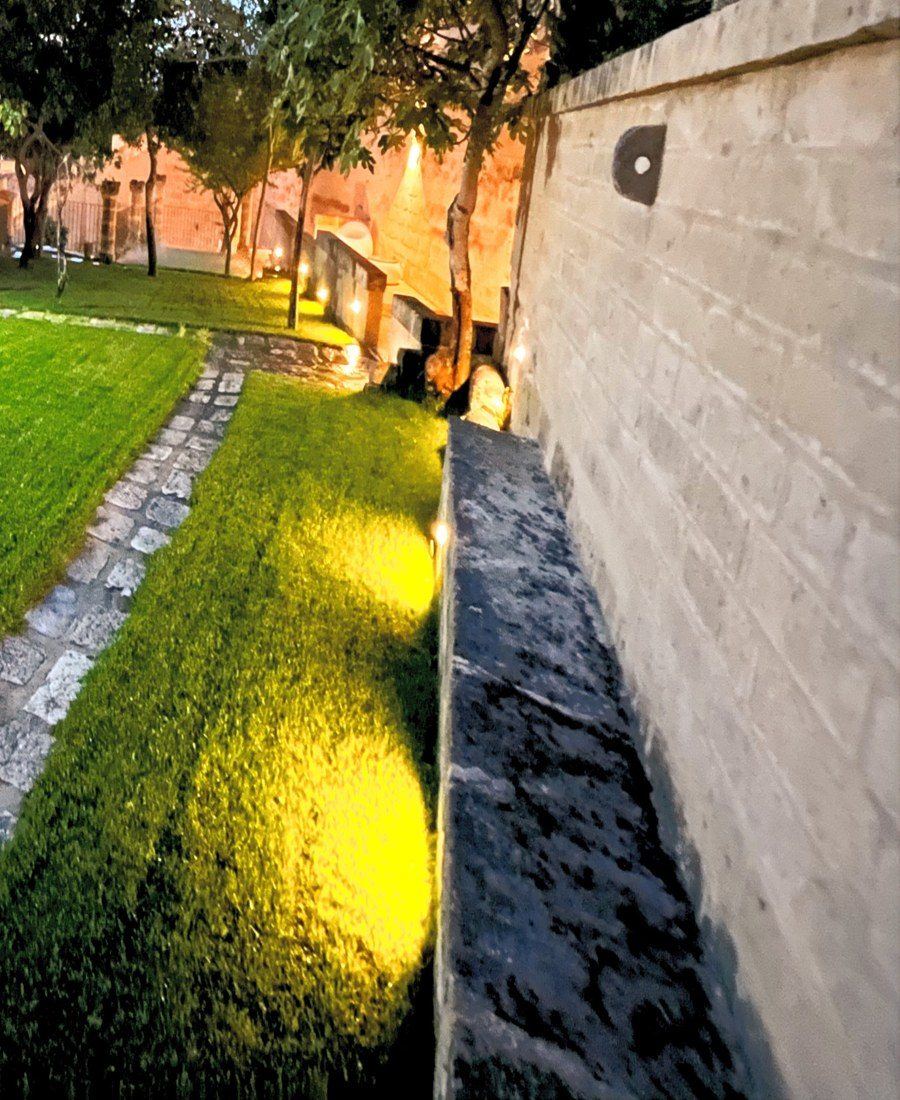 Il camminamento illuminato lungo il muro di tufo, la sera